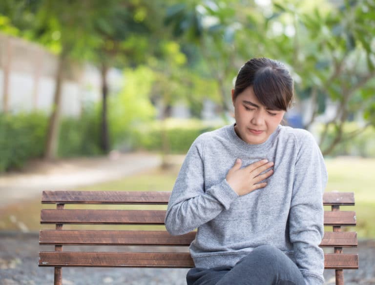 A person sitting on a bench and holding their chest in pain