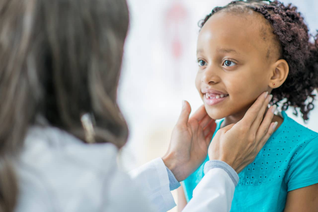 A child smiling at an ENT who's patting the sides of their throat