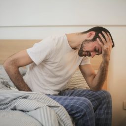 Man with a headache sitting on the edge of his bed.