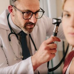 ENT doctor checking ear with otoscope of woman patient at hospital. Physician examining ear of female patient with an instrument.