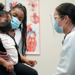 Mom and daughter visiting with their doctor, masks on.