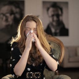 A woman using a tissue to cover her sneeze.