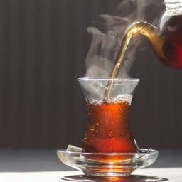 Glass cup of brewed black turkish tea pouring from teapot, traditional hot drink concept