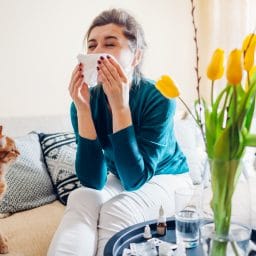 Woman with allergies sneezing next to a cat indoors.