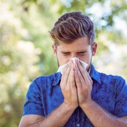 Young man blowing his nose on a sunny day.