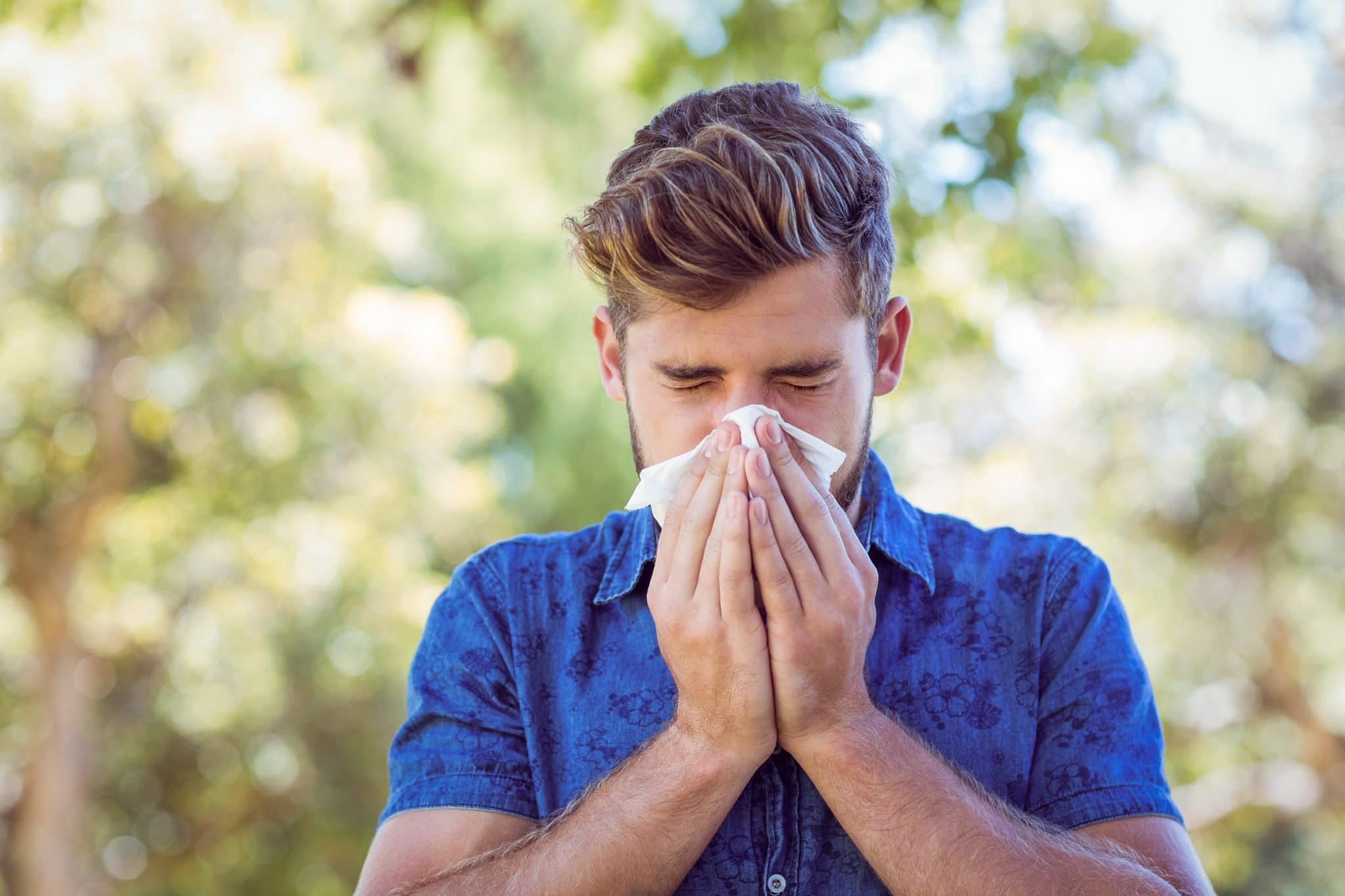 Young man blowing his nose on a sunny day.