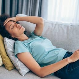 Sick young woman lying on the couch and holding her head with hand. Ill woman lying on the sofa with high temperature.