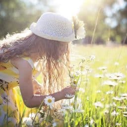 Little girl smelling flowers in a field.