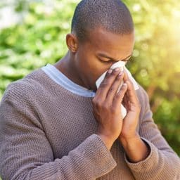 Shot of a young man blowing his nose outdoors