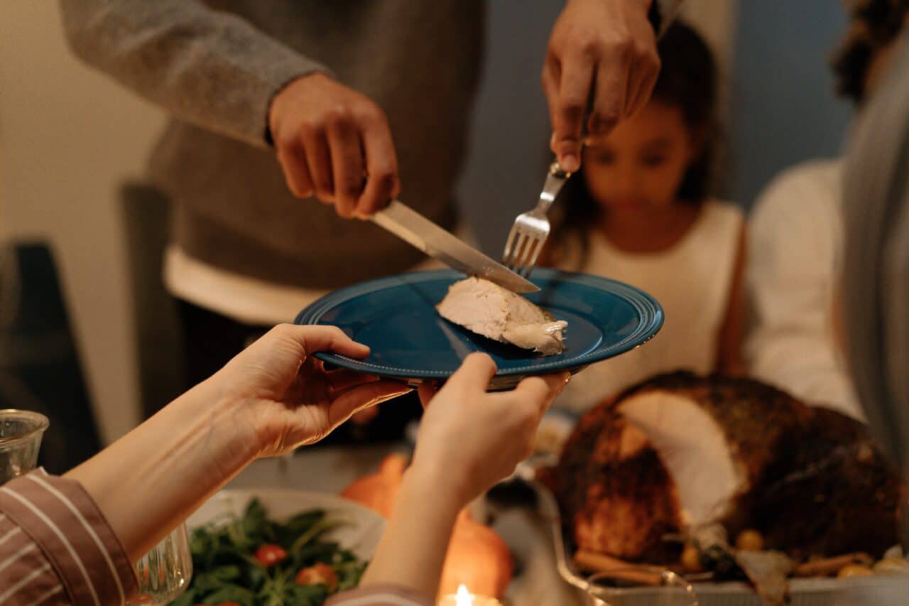 A family getting ready to eat thanksgiving together, cutting turkey on a plate.