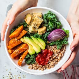 Baked vegetables, avocado, tofu and buckwheat buddha bowl. Vegan lunch salad with kale, baked sweet potato, tofu, buckwheat and avocado in a white bowl. Vegan concept.