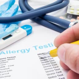 Doctor checks patient's allergy analysis near stethoscope and thermometer. Scene from work or professional activities of general practitioner, allergist, pediatrician or therapist in allergy treatment