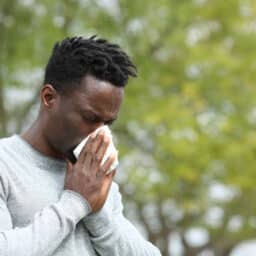 Man with allergies blowing his nose in an outdoor park.