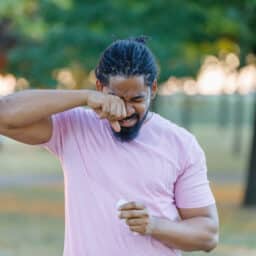 Young man with allergies rubbing his eyes outside.