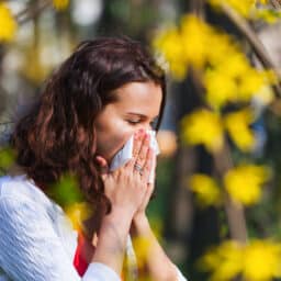 Woman blowing her nose amidst a bunch of flowers