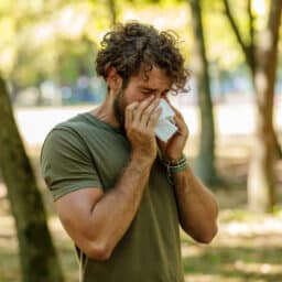 Man sneezing into a tissue at the park