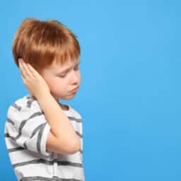 Young boy holding his ear on a blue background