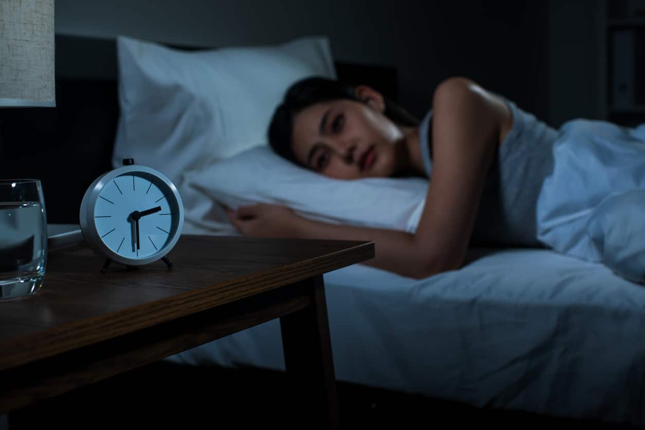 Woman lying awake in bed staring at the alarm clock.