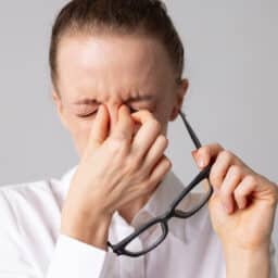 Woman with sinus pressure holding her nose bridge with glasses in the other hand