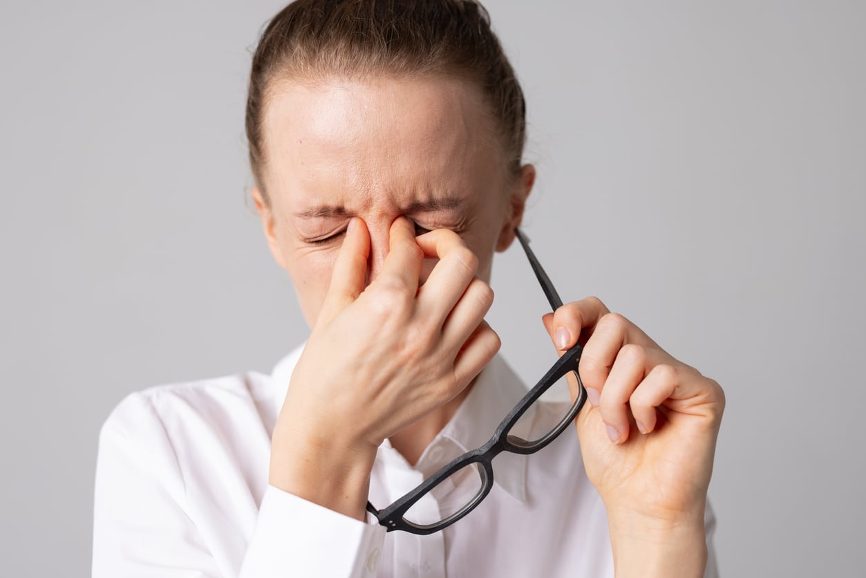 Woman with sinus pressure holding her nose bridge with glasses in the other hand.