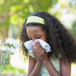 Young girl sitting by flower and blowing her nose in the park