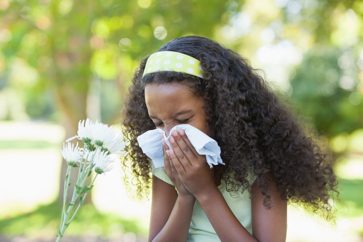 Young girl sitting by flower and blowing her nose in the park.