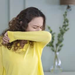 Woman sneezing into her elbow at home