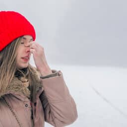 Woman holding her nose while standing out in the snowy cold.
