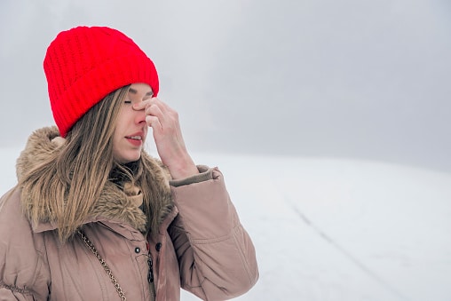 Woman holding her nose while standing out in the snowy cold.