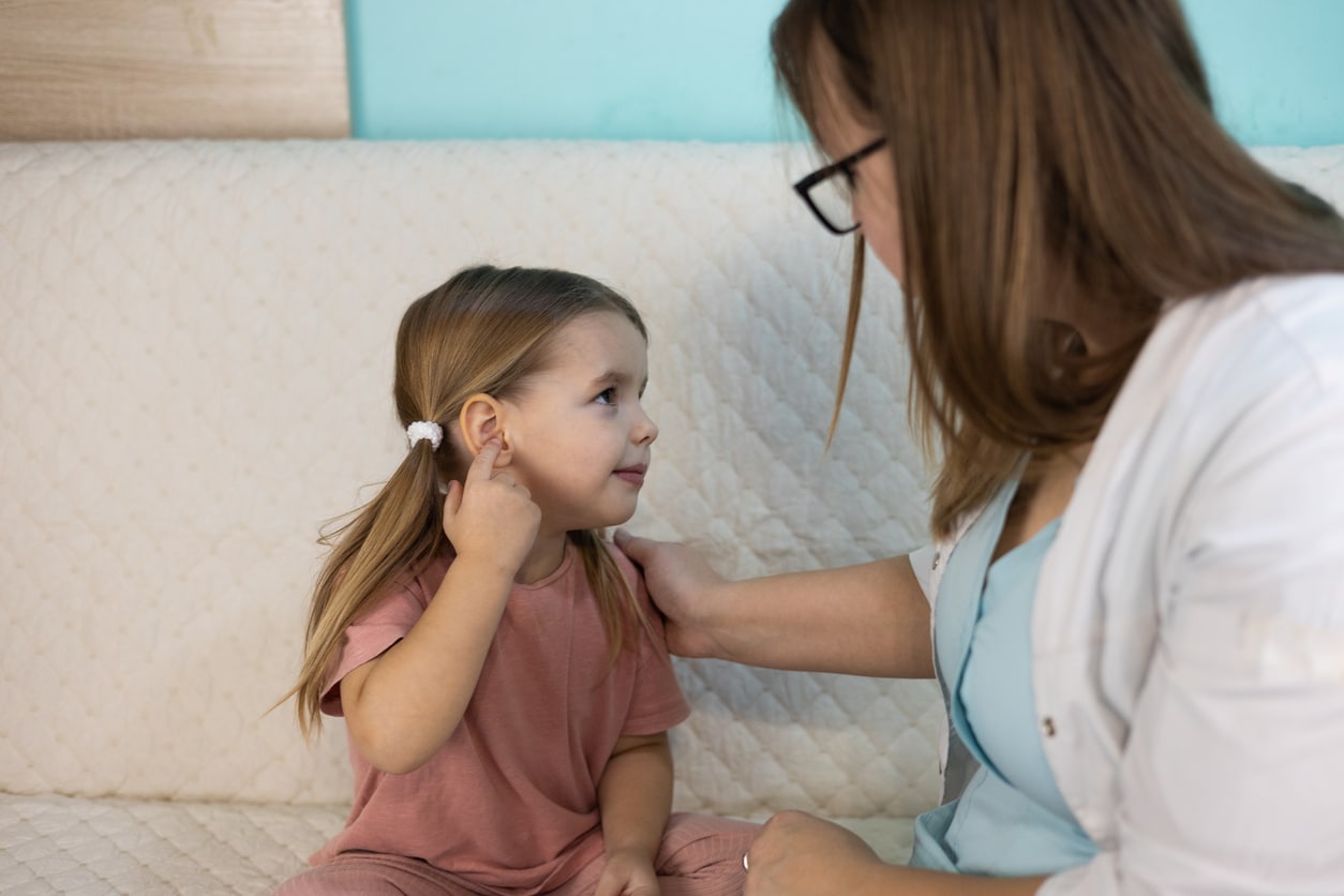 Young girl pointing at her ear to show her mom that it hurts.
