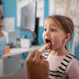 A doctor checking a little girl's throat in his office.