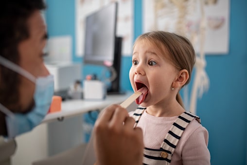 A doctor checking a little girl's throat in his office.